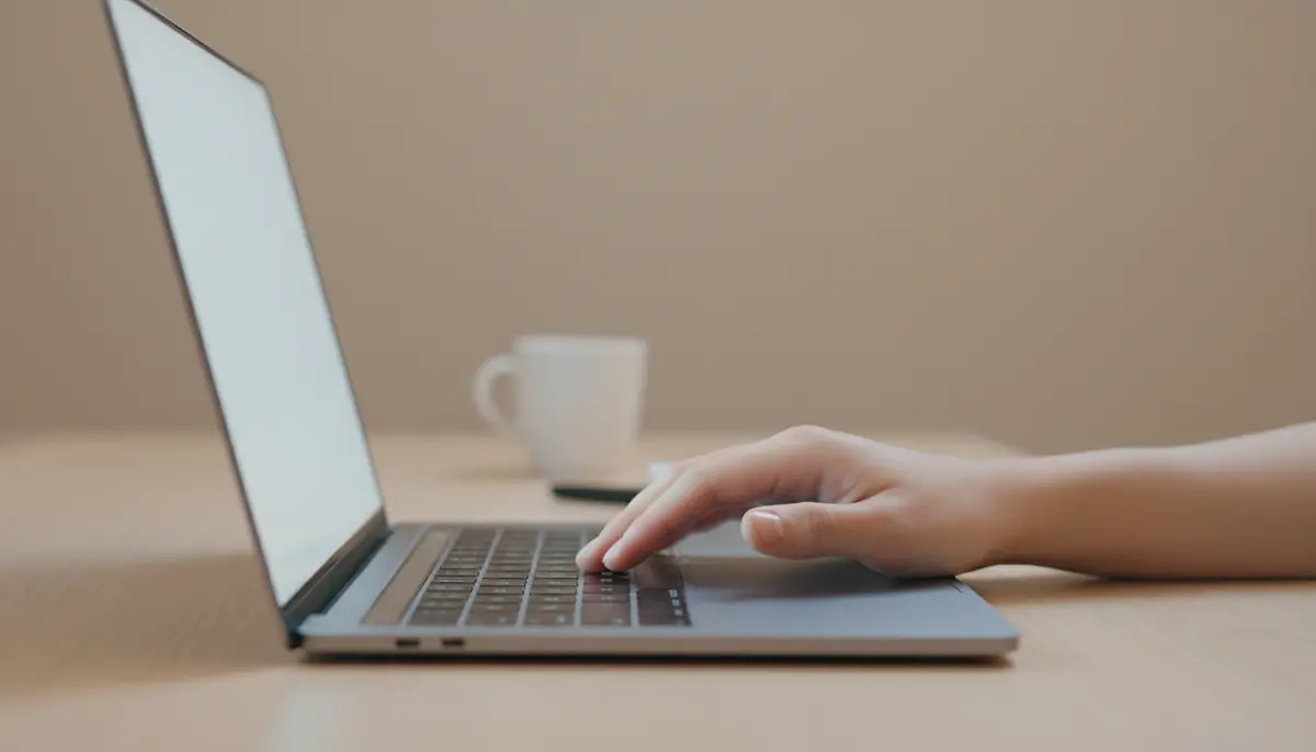 Mão suspensa sobre o trackpad de um notebook iluminada pelo brilho da tela em um quarto escuro